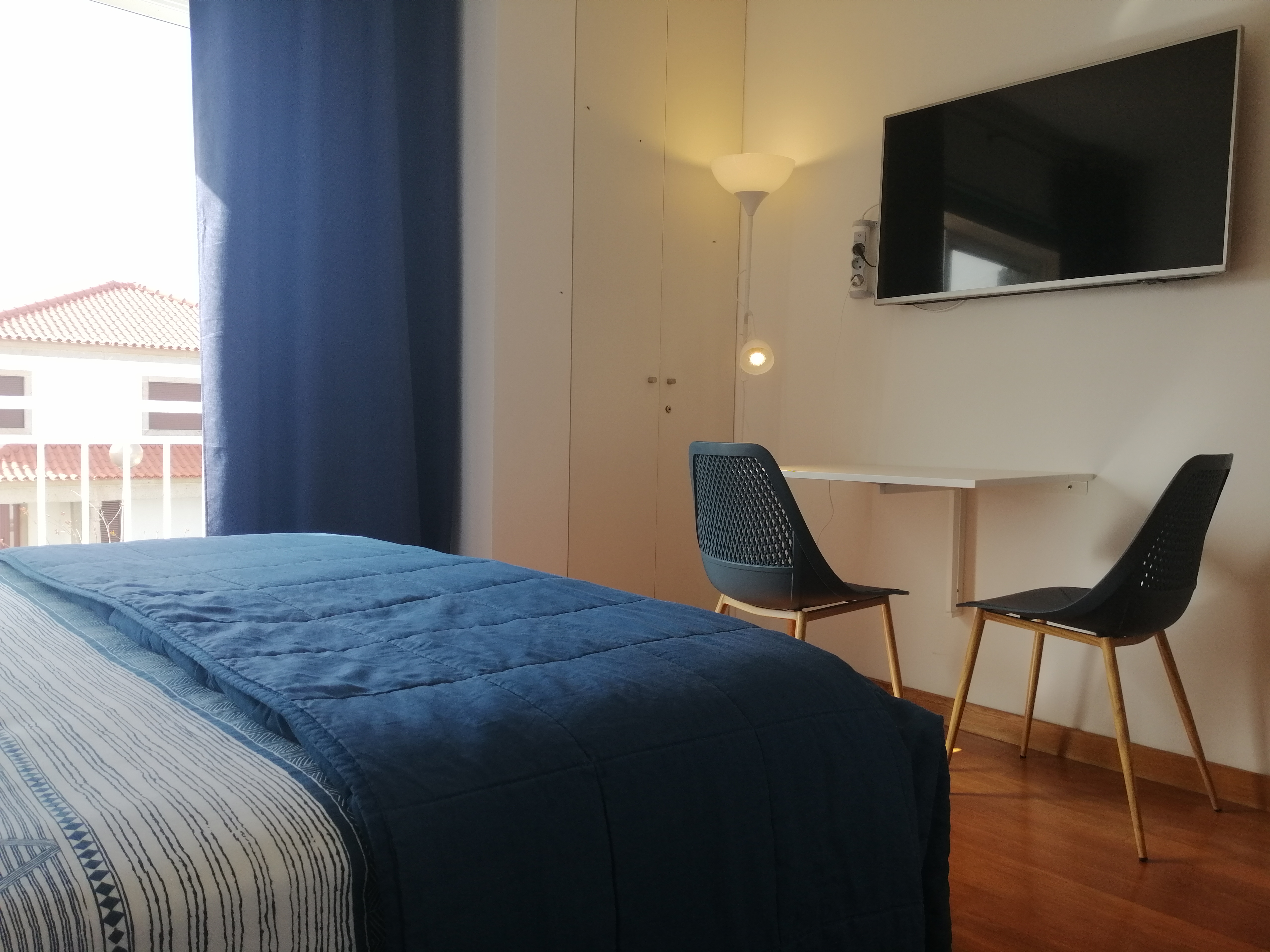 Interior da suite com cama de casal, secretária, cadeiras e televisão de ecrã plano