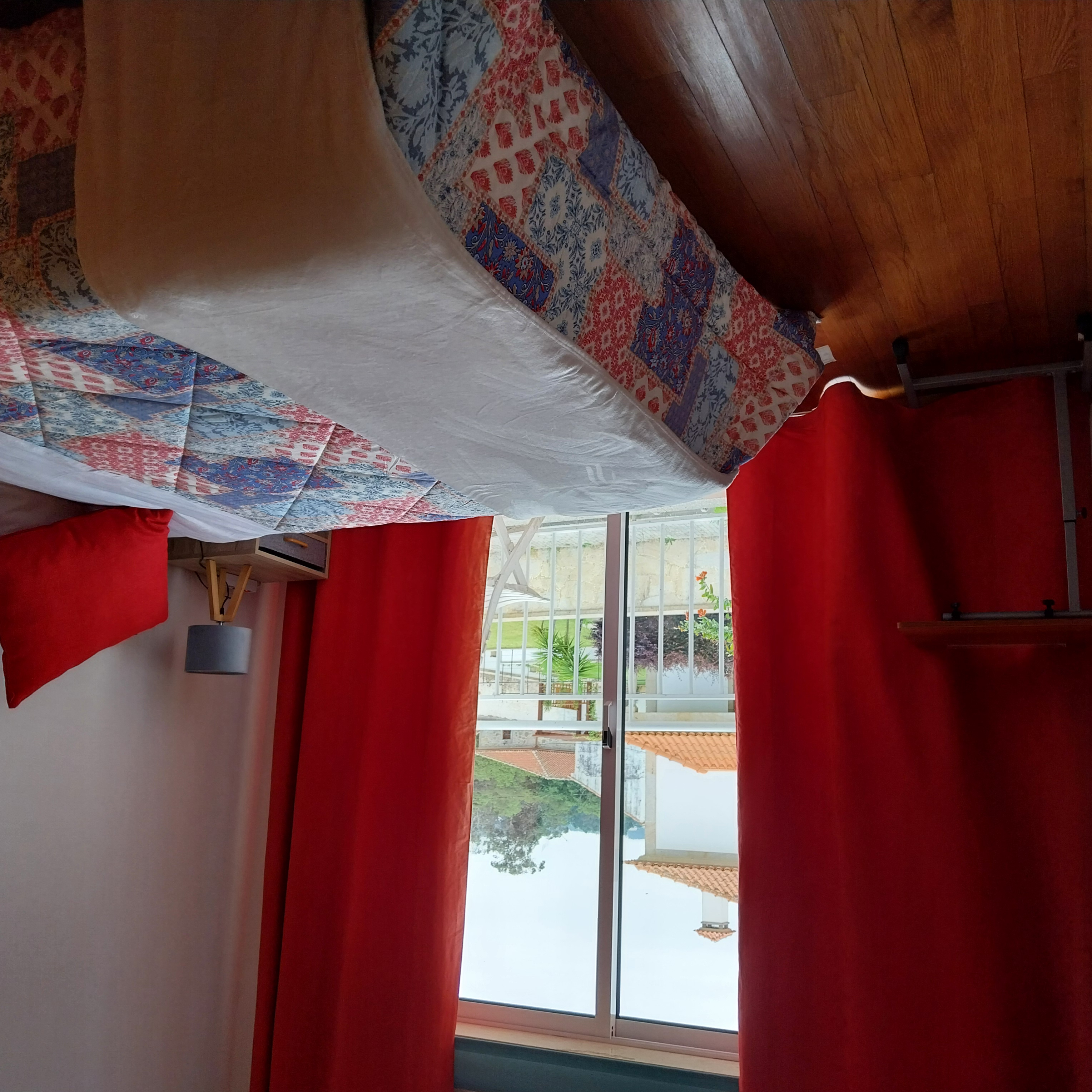 Interior do Quarto Duplo com Varanda com cortinado vermelho, mesa de apoio e vista para a varanda